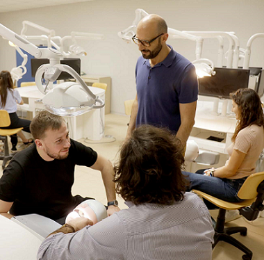 A professor is standing among students sitting in a dentistry lab of the Unievrsity of Siena
